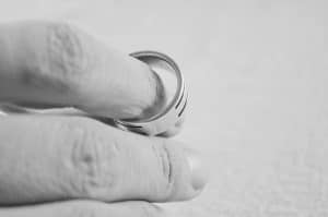 Close-up of a hand wearing a simple, smooth ring on the index finger. The black and white image highlights the texture of the skin and the metallic surface of whats now yours. divorce attorney colorado springs