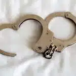 A pair of open metal handcuffs rests on a white fabric surface, subtly evoking the tension and complexities that can arise when criminal charges intertwine with the intricacies of a divorce. divorce attorney colorado springs
